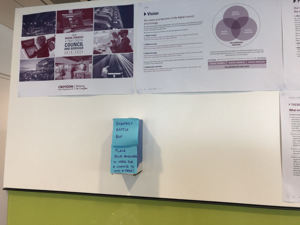 Office wall with poster explaining the Croydon Digital Strategy 'vision', with a 'strategy raffle box' underneath.