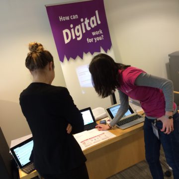 Two women looking at a computer screen next to a stand banner that reads "How can digital work for you?"