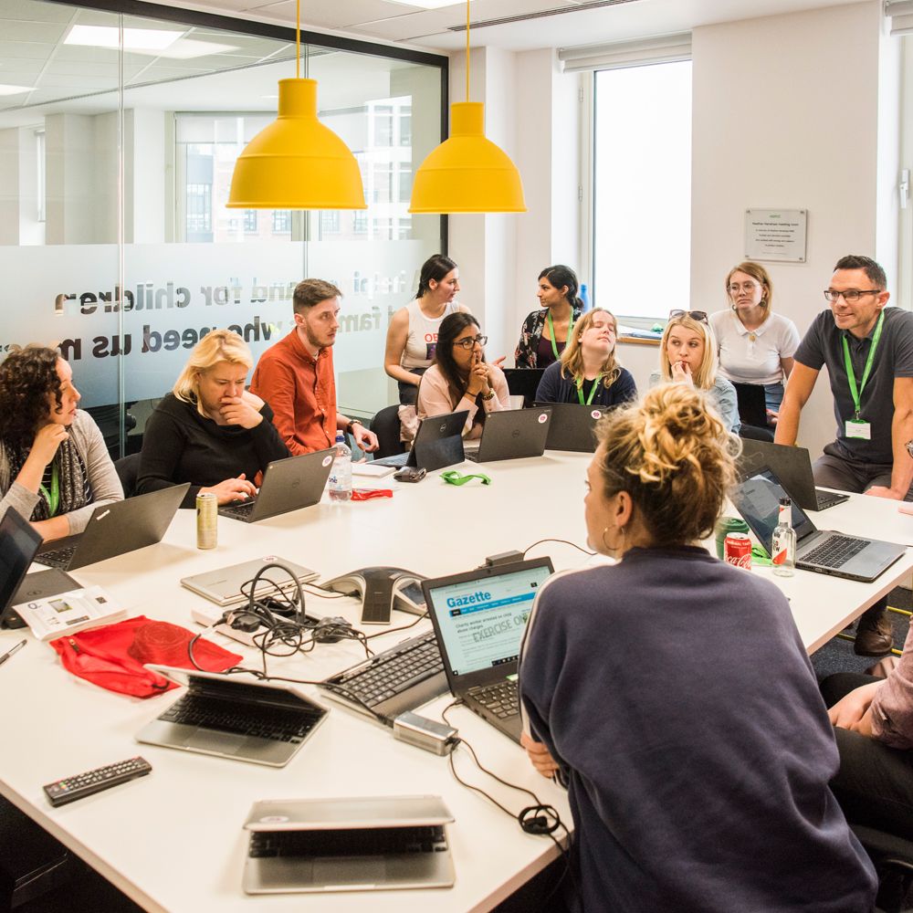 Group of people on laptops huddled round a table in a meeting room